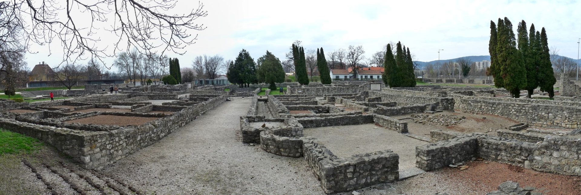 Excavated stone walls and paved streets of the Roman civil town in the Aquincum archaeological park, with the museum buildings behind